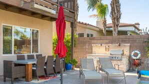 An outdoor patio with a dining table, chairs, a red umbrella, and a barbecue grill. - Ideal Summer getaway home  License #065778 (La Quinta)