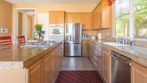 A modern kitchen with wooden cabinets, stainless steel appliances, and a granite countertop. - Ideal Summer getaway home  License #065778 (La Quinta)