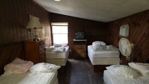 Una habitación con dos camas, una pared de madera, una ventana, un televisor y un ventilador.