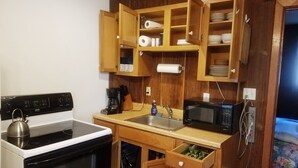 Cocina compacta con estufa, microondas, pileta y alacenas de madera.