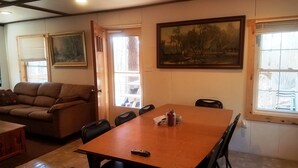 Un comedor con una mesa de madera, sillas, un control remoto y un cuadro en la pared.