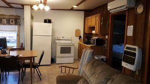 Cocina compacta con refrigerador, estufa, microondas y un pequeño comedor con mesa y sillas.