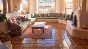 Un salón acogedor con un sofá curvo, una mesa de centro y una chimenea. Amplias ventanas ofrecen vistas al exterior.