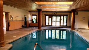 Una piscina interior con vigas de madera, ventanas de vidrio transparente y una escalera de metal.