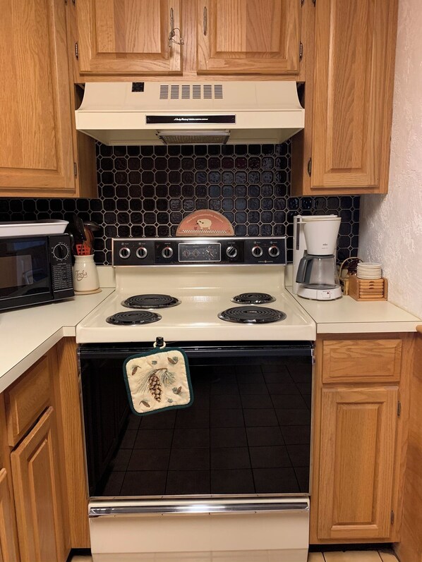 Kitchen area with stove, microwave, and coffee maker, featuring wooden cabinets and a tiled backsplash.