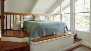 Une chambre à coucher avec un lit en bois, des murs blancs et une grande fenêtre.