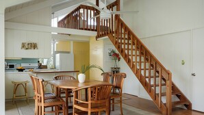 Un vaste espace dédié à la salle à manger, avec une table et des chaises en bois, un escalier et une cuisine en arrière-plan.