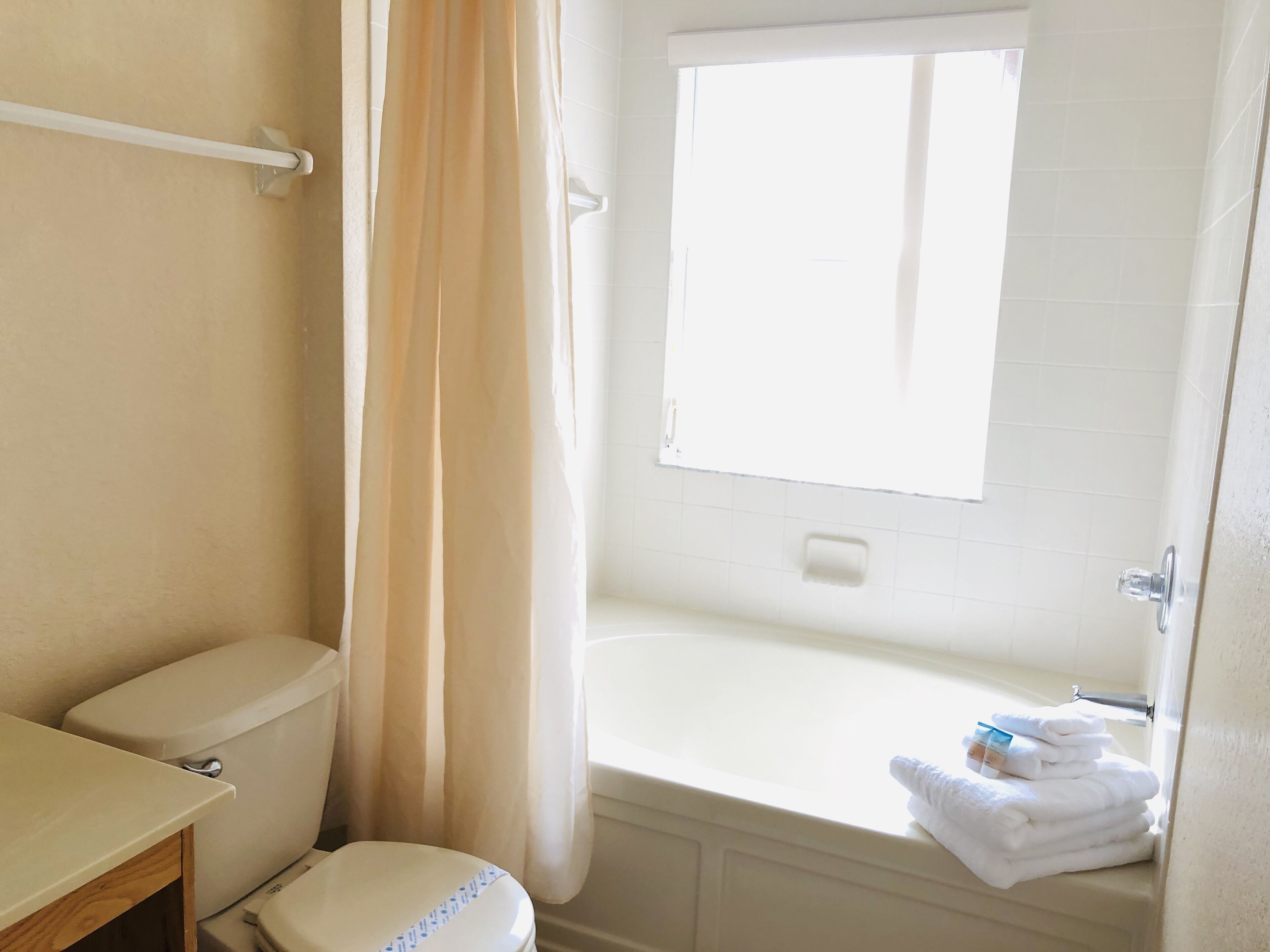 A bathroom with a toilet, a bathtub, a window, and a towel rack.