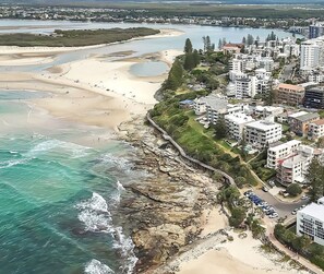 An aerial view of a coastal area with a beach, rocky shoreline, and residential buildings.
