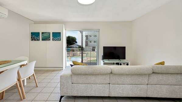 A modern living room with a sofa, a TV, and a dining area with chairs and a table. - Beachcomber Unit 4, 7 Dingle Ave (KINGS BEACH)
