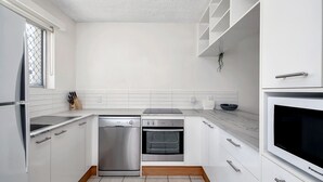 Cozinha moderna com armários brancos, lava-louças, forno e micro-ondas embutido.
