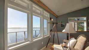 A room with large windows overlooking a body of water, a tripod with a lamp, and a seating area with patterned cushions. - Bird Watch @ Land's End with Amazing Views of the Harbor and Pacific Ocean (Bodega Bay)