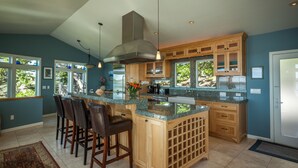 A spacious kitchen with a large island, bar stools, wooden cabinets, and a view of the outdoors. - Bird Watch @ Land's End with Amazing Views of the Harbor and Pacific Ocean (Bodega Bay)