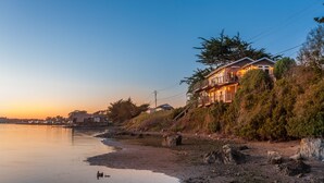A coastal property with a large house featuring a balcony, situated on a rocky shoreline with a view of the sea. - Bird Watch @ Land's End with Amazing Views of the Harbor and Pacific Ocean (Bodega Bay)