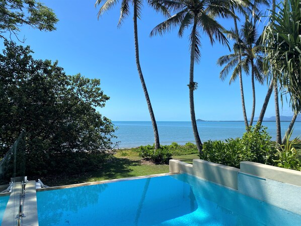 A swimming pool with a clear view of the ocean and palm trees.