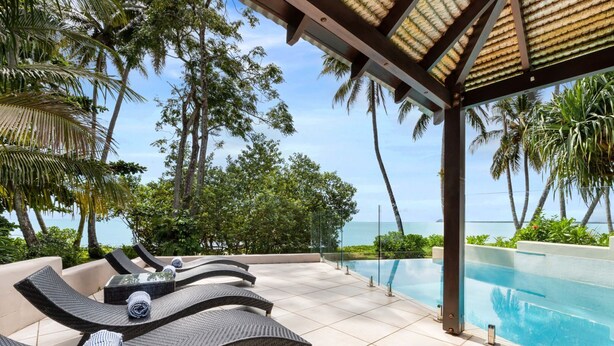 A poolside area with lounge chairs, a tiled floor, and a view of the ocean.