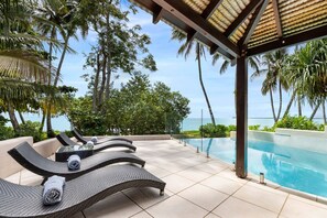A poolside area with lounge chairs, a tiled floor, and a view of the ocean.