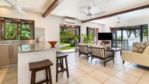 A modern kitchen with a central island, bar stools, a dining area with a sofa, and a TV.