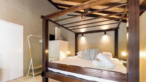 A four-poster bed with a wooden frame, a white mattress, and a neatly made bed with white linens and a patterned pillow.