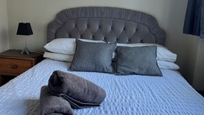 A neatly made bed with a grey headboard, white pillows, and a folded grey towel on the bed.