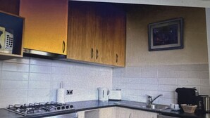 A kitchen with wooden cabinets, a gas stove, a coffee maker, and a framed picture on the wall.