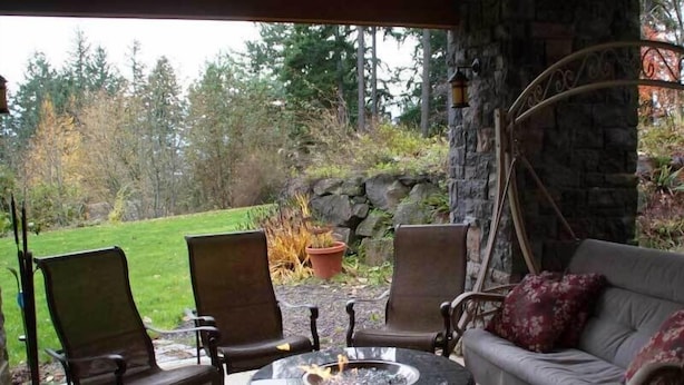 Een terras buiten met een ronde tafel, twee stoelen en een bank.