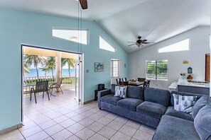 A spacious living area with a large gray sofa, a dining table, and a view of the ocean through a sliding glass door.