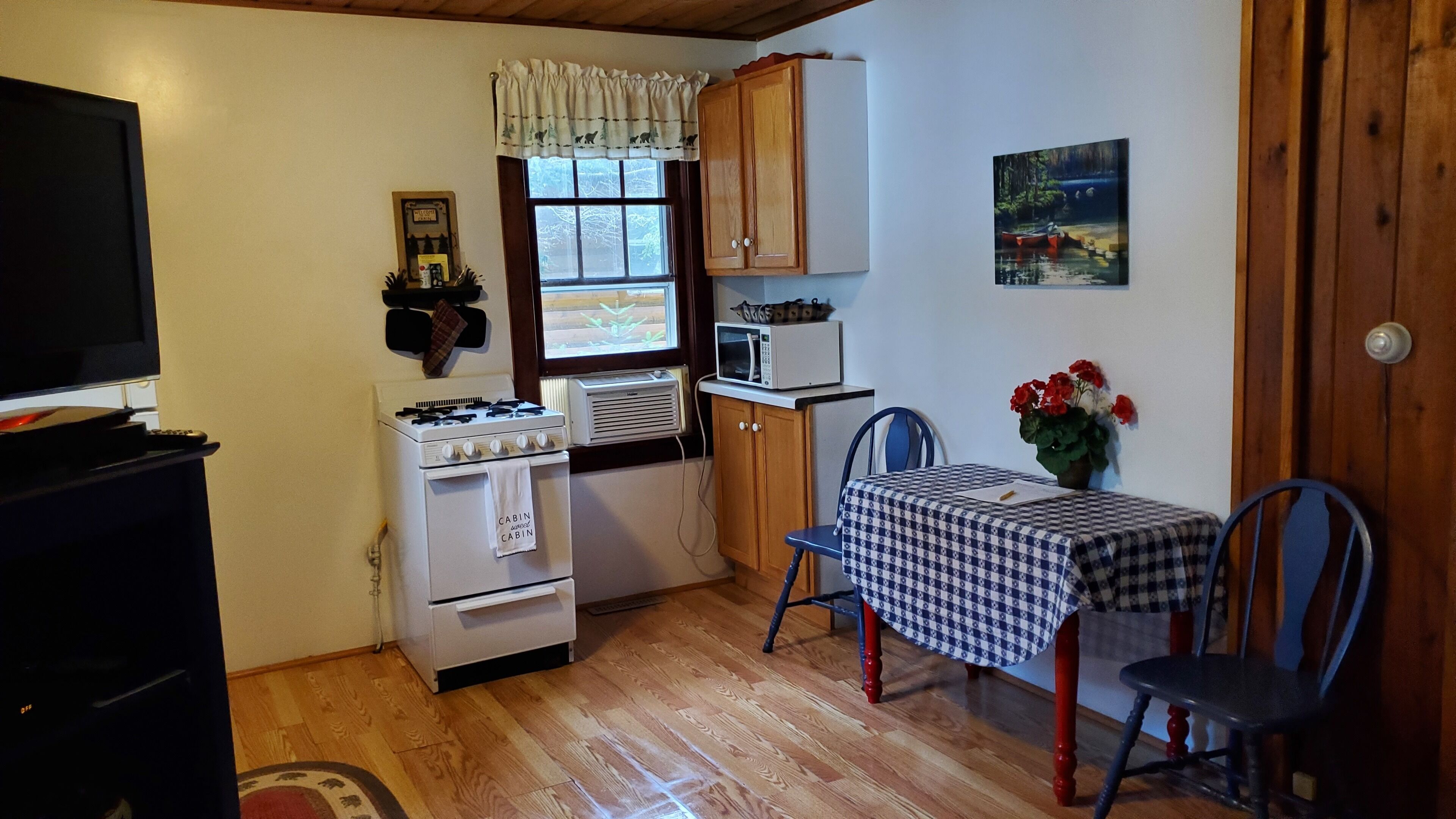 Una cocina compacta con estufa, microondas y armarios. Hay una mesa de comedor con sillas y un cuadro en la pared.