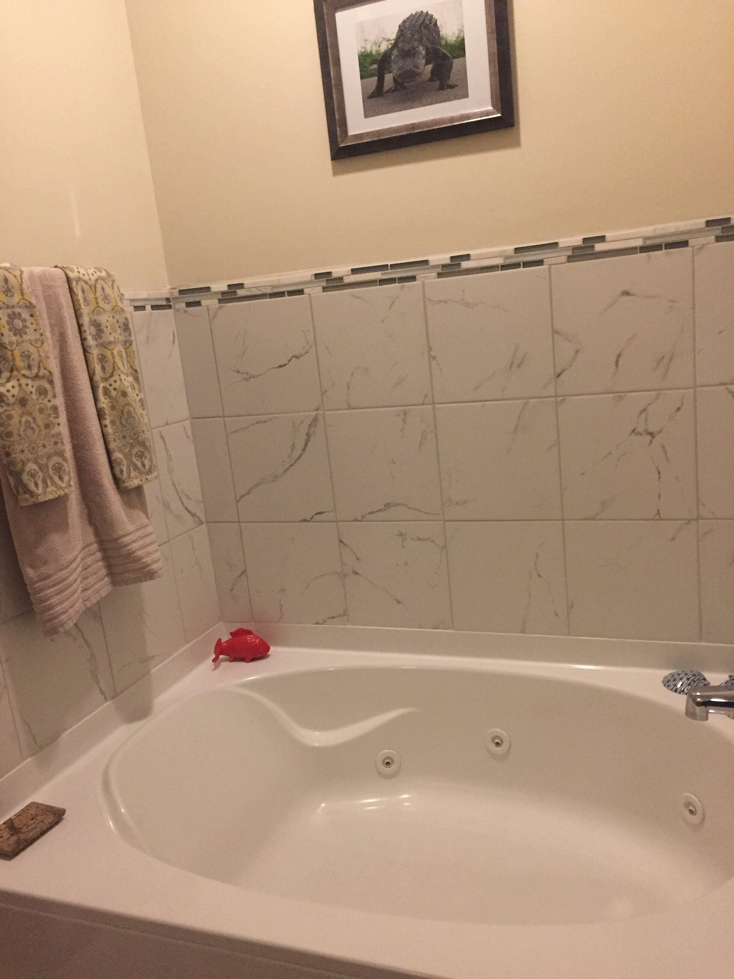 A bathroom with a marble-tiled wall, a bathtub, and a framed picture above the tub.