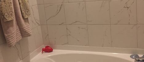 A bathroom with a marble-tiled wall, a bathtub, and a framed picture above the tub.