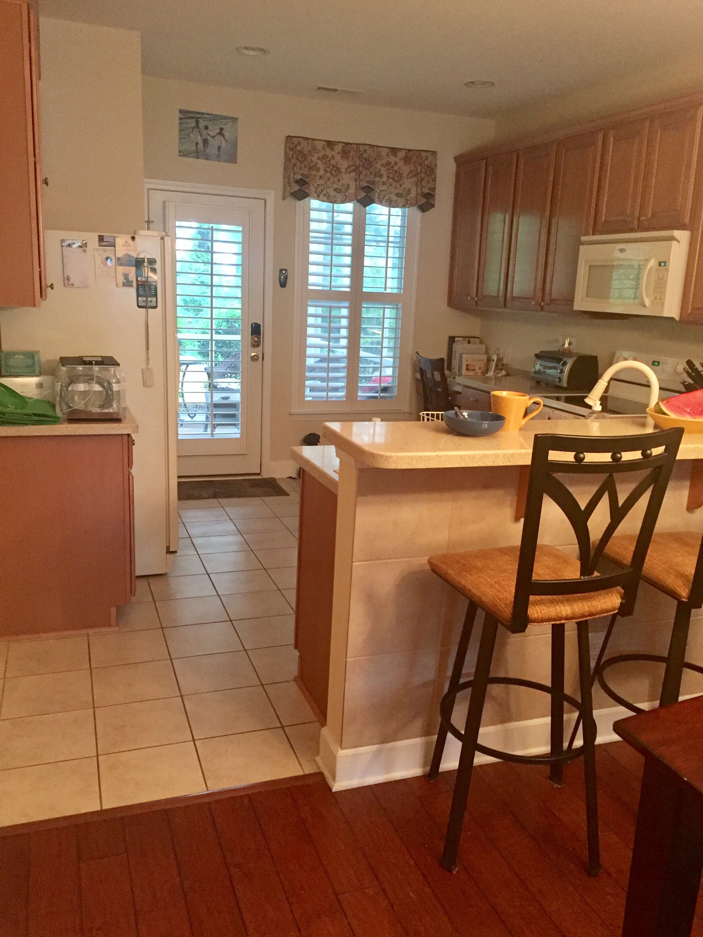 A kitchen with wooden cabinets, a microwave, a sink, and a window with blinds.