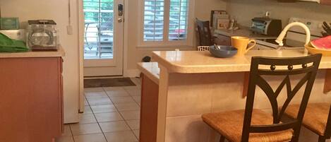 A kitchen with wooden cabinets, a microwave, a sink, and a window with blinds.