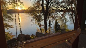 A wooden swing overlooking a lake with trees and rocks. - Remodeled Log Cabin Home Chain of Lakes (Alexandria)