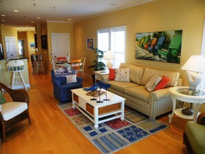 Uma sala de estar com um sofá listrado, uma poltrona azul, uma mesa de centro e uma área de jantar com mesa e cadeiras.