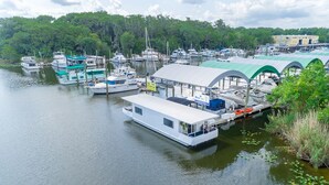 A marina with several boats docked, a covered boat house, and a building with a green roof in the background.