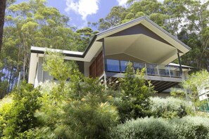 Una casa moderna con un balcón grande, rodeada de abundante vegetación.