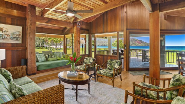 A spacious living area with wicker furniture, a ceiling fan, and large windows offering a view of the ocean. - Wilikoki - a 6br/3ba beachfront home on Hanalei Bay (Hanalei)