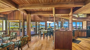 A spacious dining area with wooden flooring and large windows offering a view of the sea. - Wilikoki - a 6br/3ba beachfront home on Hanalei Bay (Hanalei)