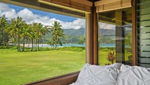 A bedroom with a large window overlooking a tropical landscape with palm trees and a beach. - Wilikoki - a 6br/3ba beachfront home on Hanalei Bay (Hanalei)