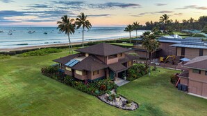 A two-story house with a large front lawn, a garage, and a view of the ocean. - Wilikoki - a 6br/3ba beachfront home on Hanalei Bay (Hanalei)