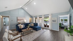 A spacious living room with a blue sectional sofa, a wooden coffee table, and a view of a backyard with a pool. - Family Dream Home, Arcade fun!, Huge Pool! 5 bedrooms, 3 baths  (Plano)