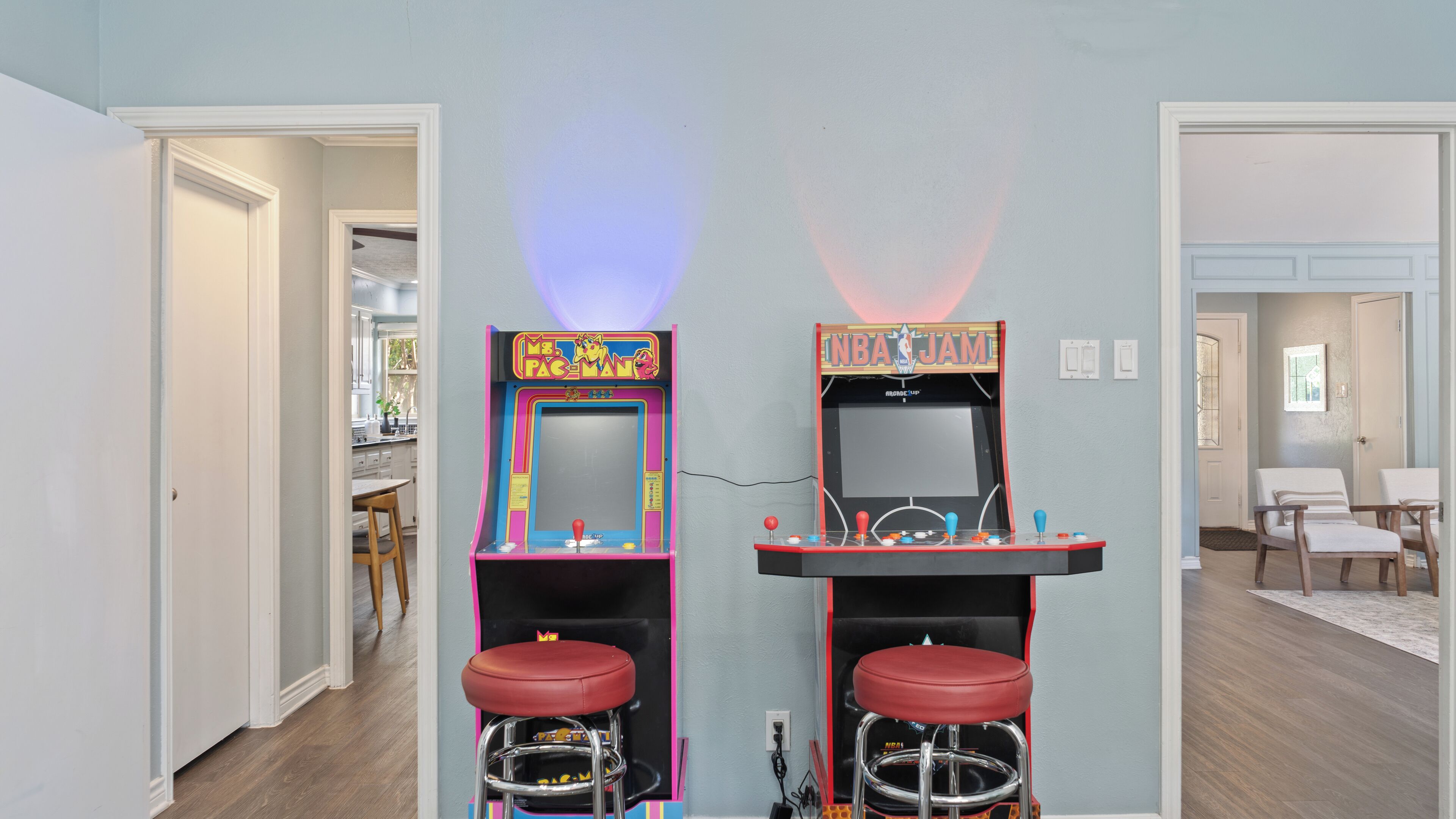Two arcade machines in a hallway with a kitchen in the background.