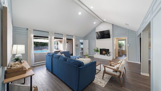 A spacious living room with a blue sectional sofa, a fireplace, and a TV mounted on the wall. - Family Dream Home, Arcade fun!, Huge Pool! 5 bedrooms, 3 baths  (Plano)