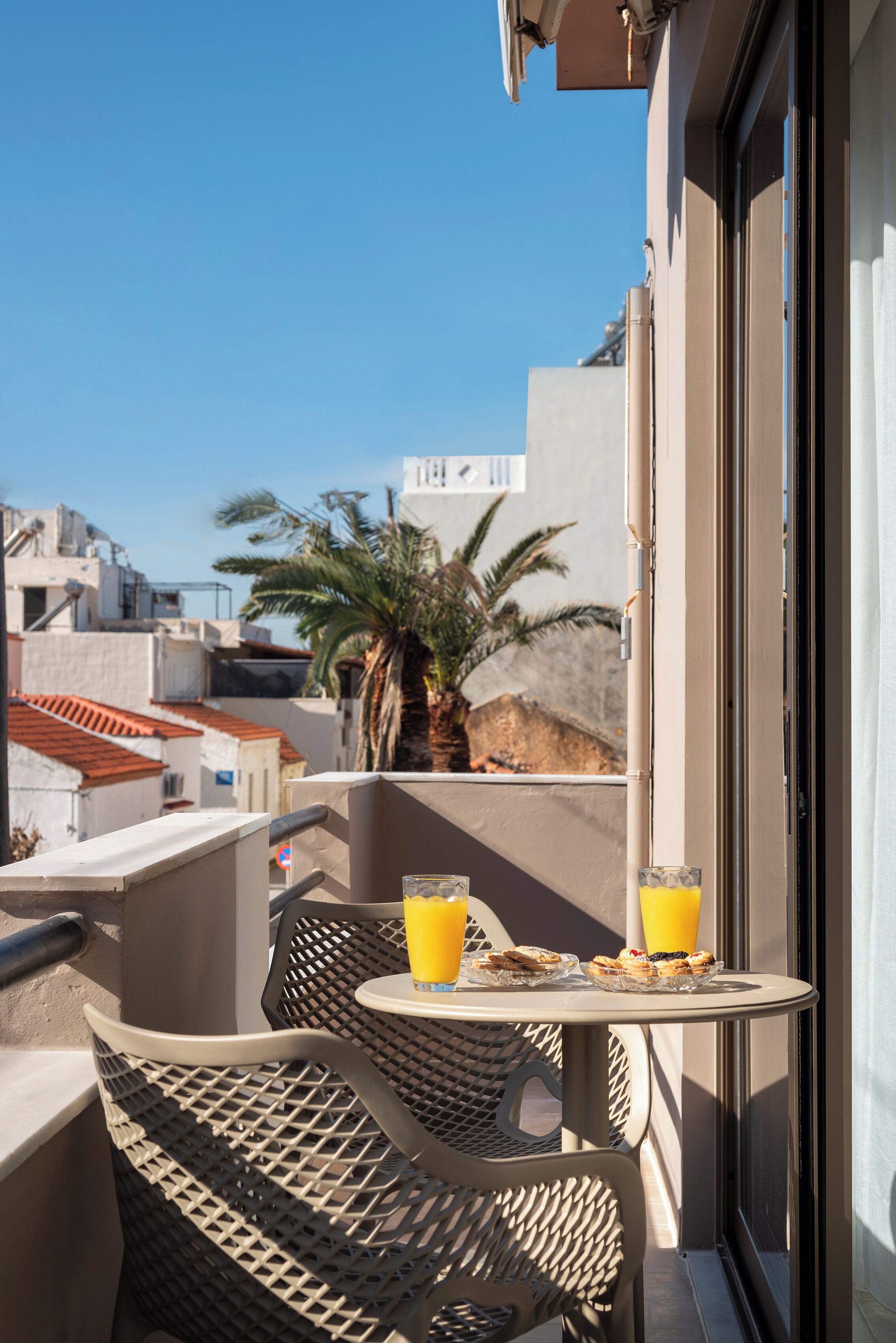 A balcony with a table and chairs, two glasses of orange juice, and a palm tree in the background.