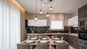 A modern kitchen with a dining area, featuring a large island, built-in appliances, and pendant lighting. - Mirma Luxury Apartment (Chania)