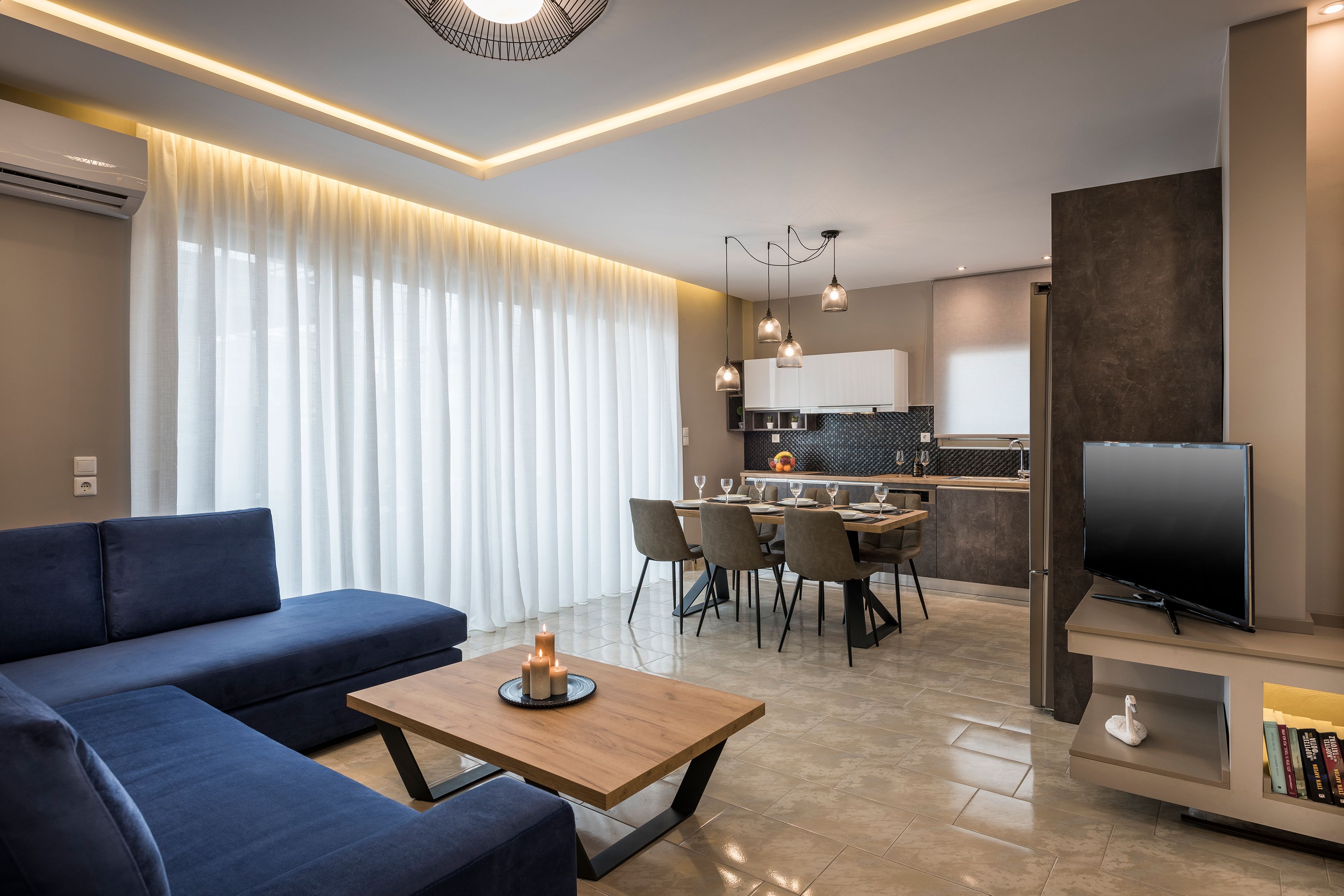 Ein modernes Wohnzimmer mit Sofa, Couchtisch und Fernseher. Es gibt einen Essbereich mit Stühlen und einem Tisch.