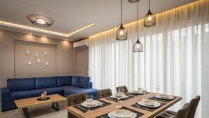 A modern dining area with a wooden table set for six, a blue sofa, and pendant lighting. - Mirma Luxury Apartment (Chania)