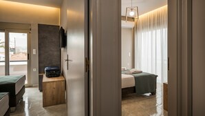 A modern hotel room with a bed, a wooden bench, a suitcase, and a television on the wall. - Mirma Luxury Apartment (Chania)