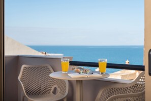 A balcony with a table, two glasses of orange juice, and a pair of glasses on a book. - Mirma Luxury Apartment (Chania)