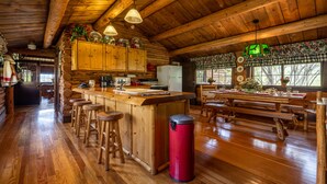 A rustic cabin-style kitchen with wooden beams, a bar area with stools, and a dining table set for four. - Double L Bar Lodge Guest Ranch (Cody)